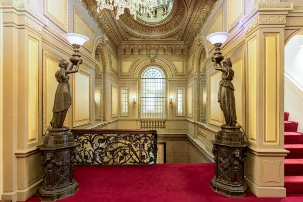 Rijk versierde trapopgang in Keizersgracht 452 met rode loper, bronzen beelden, sierlijke balustrade en groot glas-in-loodraam.