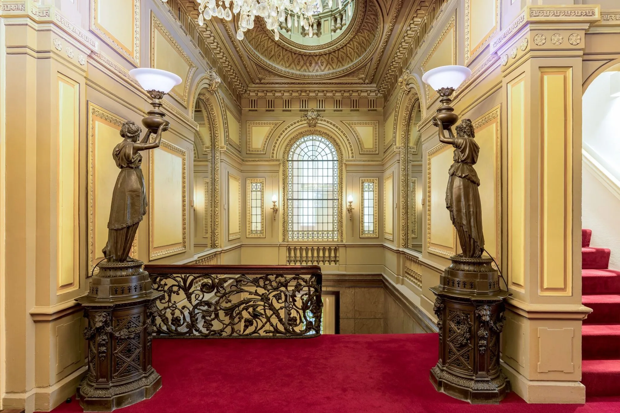 Rijk versierde trapopgang in Keizersgracht 452 met rode loper, bronzen beelden, sierlijke balustrade en groot glas-in-loodraam.