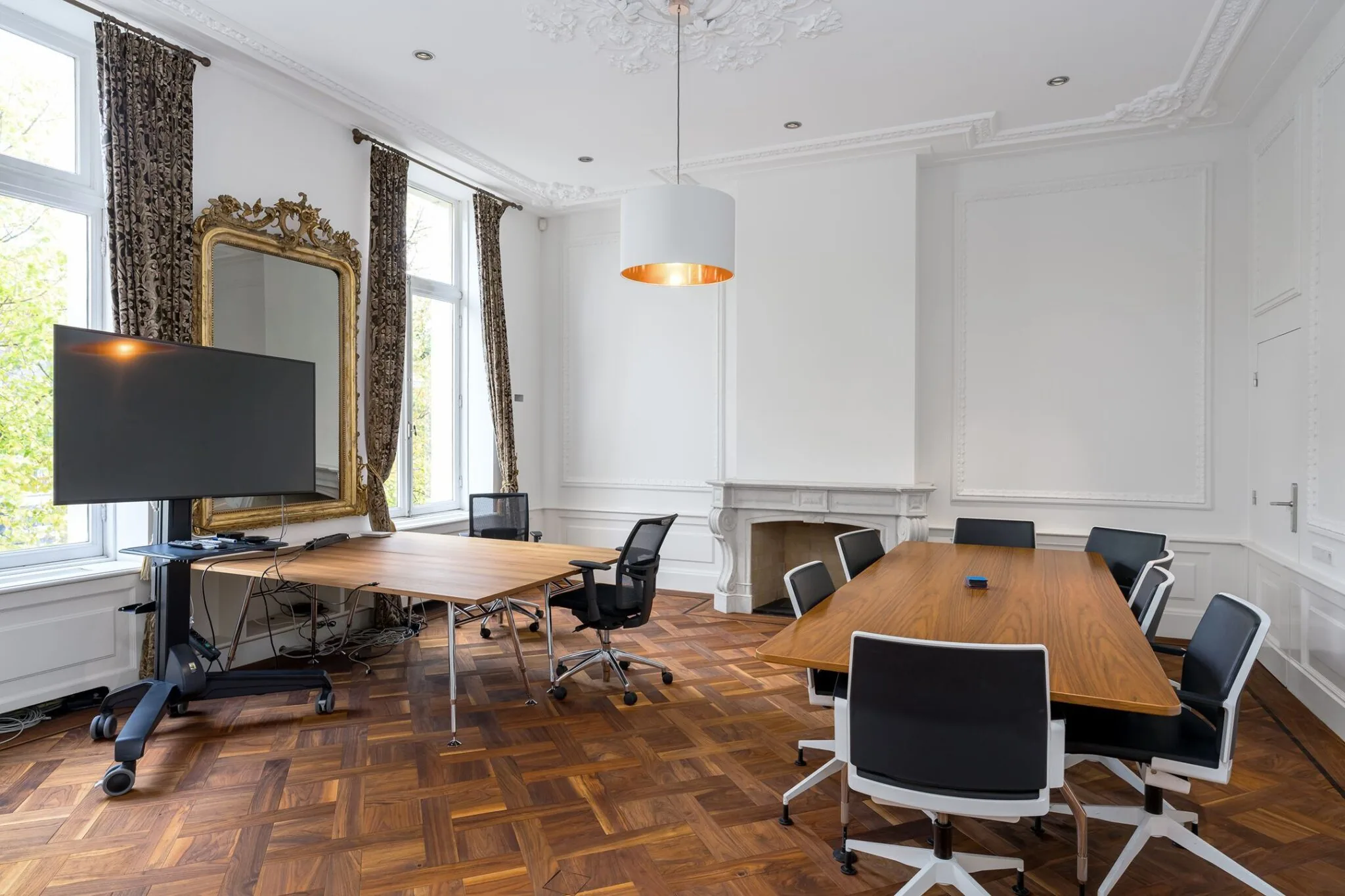 Vergaderruimte aan de Keizersgracht 452 met moderne tafels, bureaustoelen, een grote spiegel, tv-scherm en sierlijke wand- en plafondafwerking.
