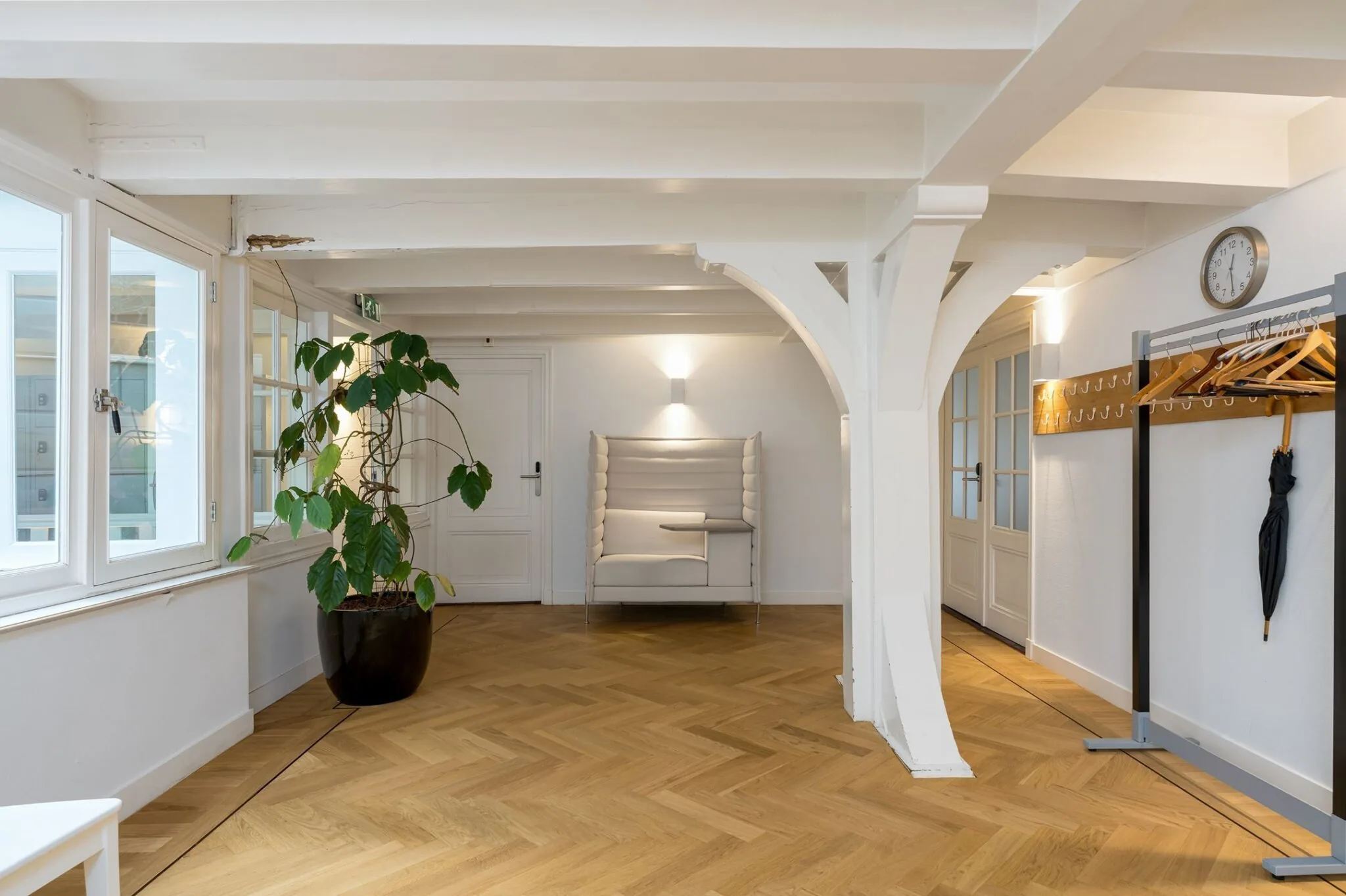 Lichte entree of hal in Keizersgracht 452 met houten visgraatvloer, kapstok, plant en moderne zitbank.