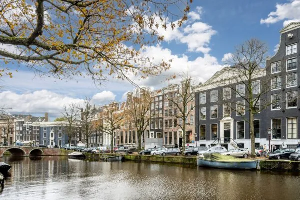 Gevels van historische grachtenpanden aan de Keizersgracht in Amsterdam met boten op het water en herfstbladeren aan de bomen.