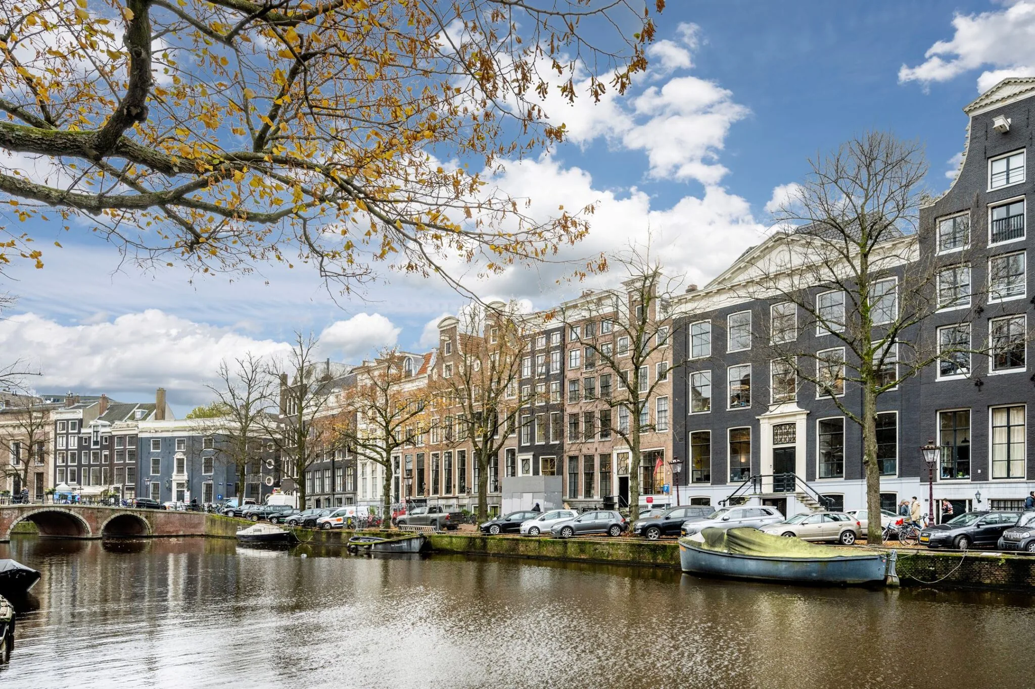 Gevels van historische grachtenpanden aan de Keizersgracht in Amsterdam met boten op het water en herfstbladeren aan de bomen.