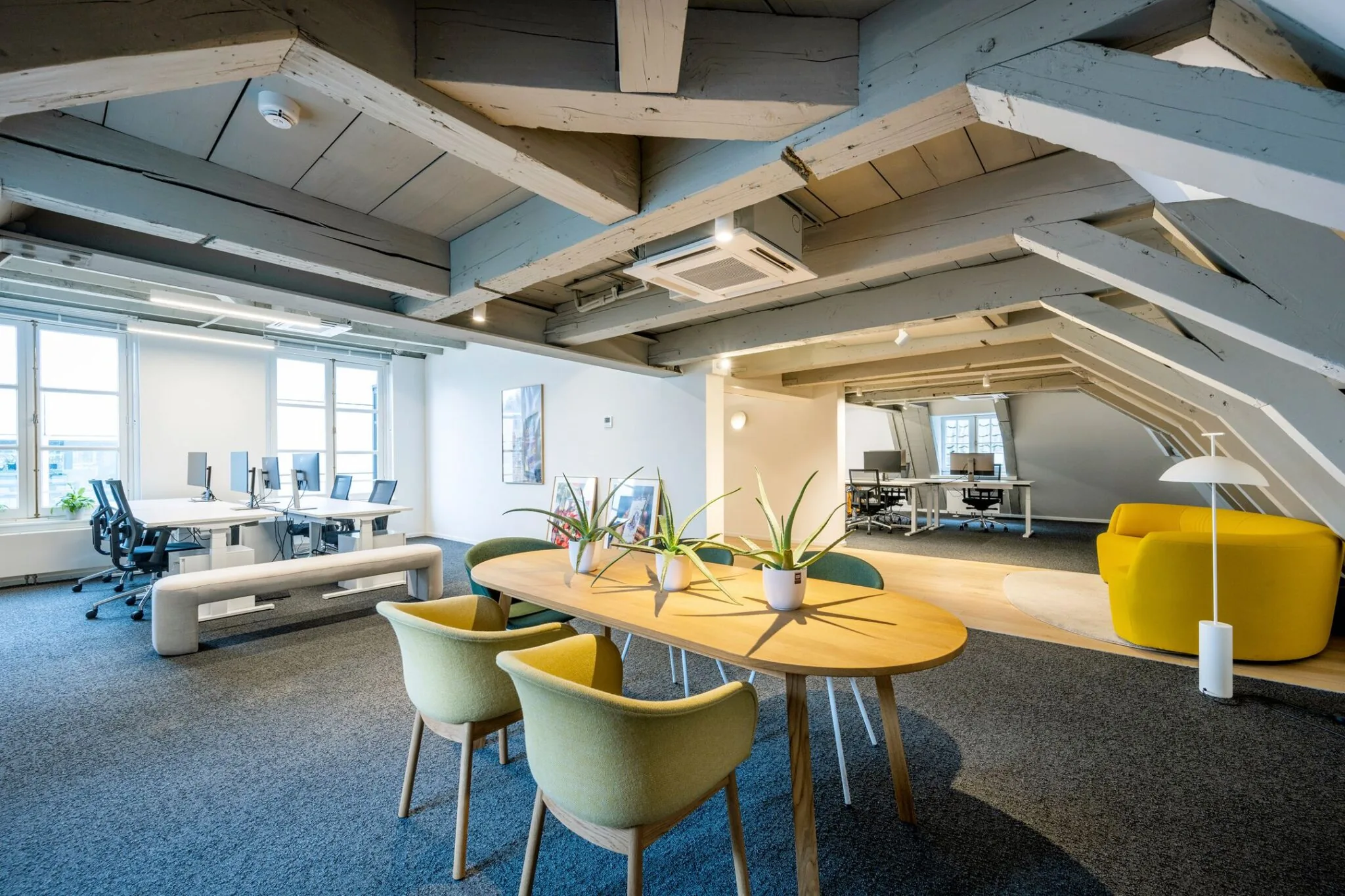 Modern kantoorinterieur op zolderverdieping van Keizersgracht 572 met werkplekken, een vergadertafel en een gele loungefauteuil.