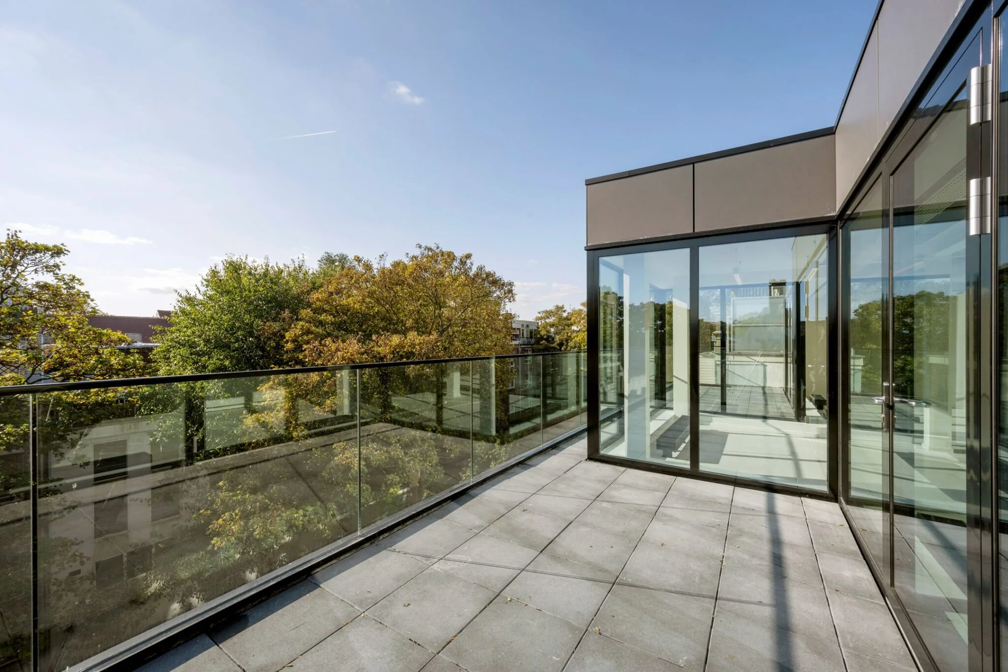 Modern dakterras met glazen balustrade en uitzicht op bomen aan de Keizersgracht 572.