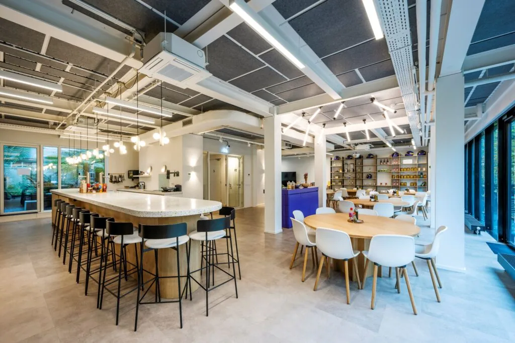 Moderne, open kantoorkeuken en kantineruimte aan de Keizersgracht 572 met een groot kookeiland, ronde eettafels en strakke verlichting.