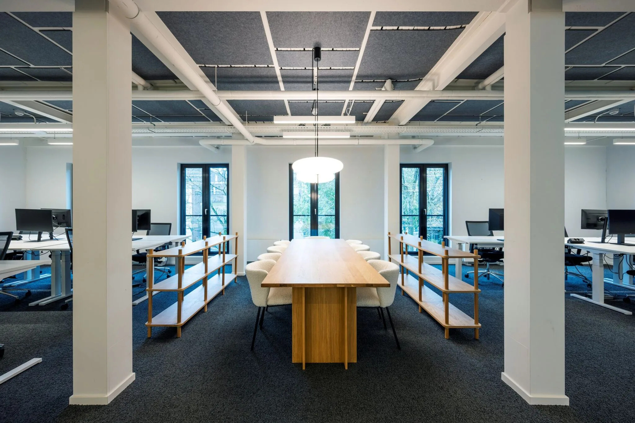 Moderne vergaderruimte in Keizersgracht 572 met lange houten tafel, omringd door stoelen en open werkplekken op de achtergrond.
