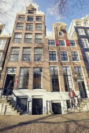 Voorgevel van het monumentale grachtenpand Keizersgracht 64 in Amsterdam met twee personen op de stoep.