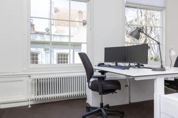 Modern kantoor met dubbele monitoren en bureaustoel bij een groot raam aan de Keizersgracht 64.