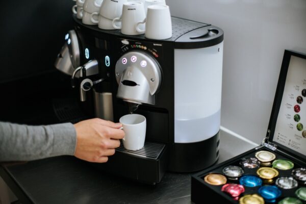 Persoon maakt koffie met een Nespresso-apparaat bij Keizersgracht 64, met een capsulehouder op het aanrecht.