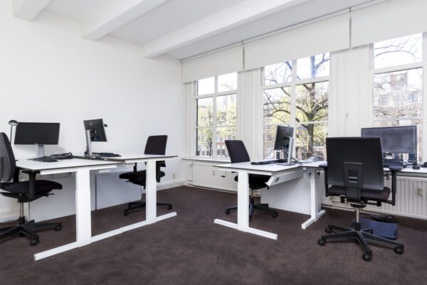 Modern kantoorinterieur op Keizersgracht 64 met vier werkplekken en grote ramen met uitzicht op de gracht.