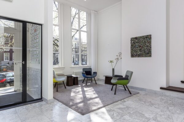 Moderne wachtruimte bij Keizersgracht 64 met kleurrijke stoelen, hoog plafond en grote ramen.