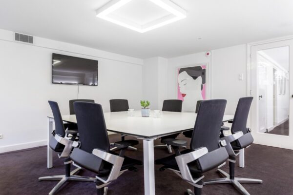 Moderne vergaderruimte in Keizersgracht 64 met wit vierkant tafel, zwarte stoelen, flatscreen en kunstwerk aan de muur.