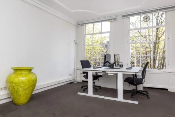 Modern kantoor met twee werkplekken, grote ramen en een opvallende groene vaas in Keizersgracht 64.
