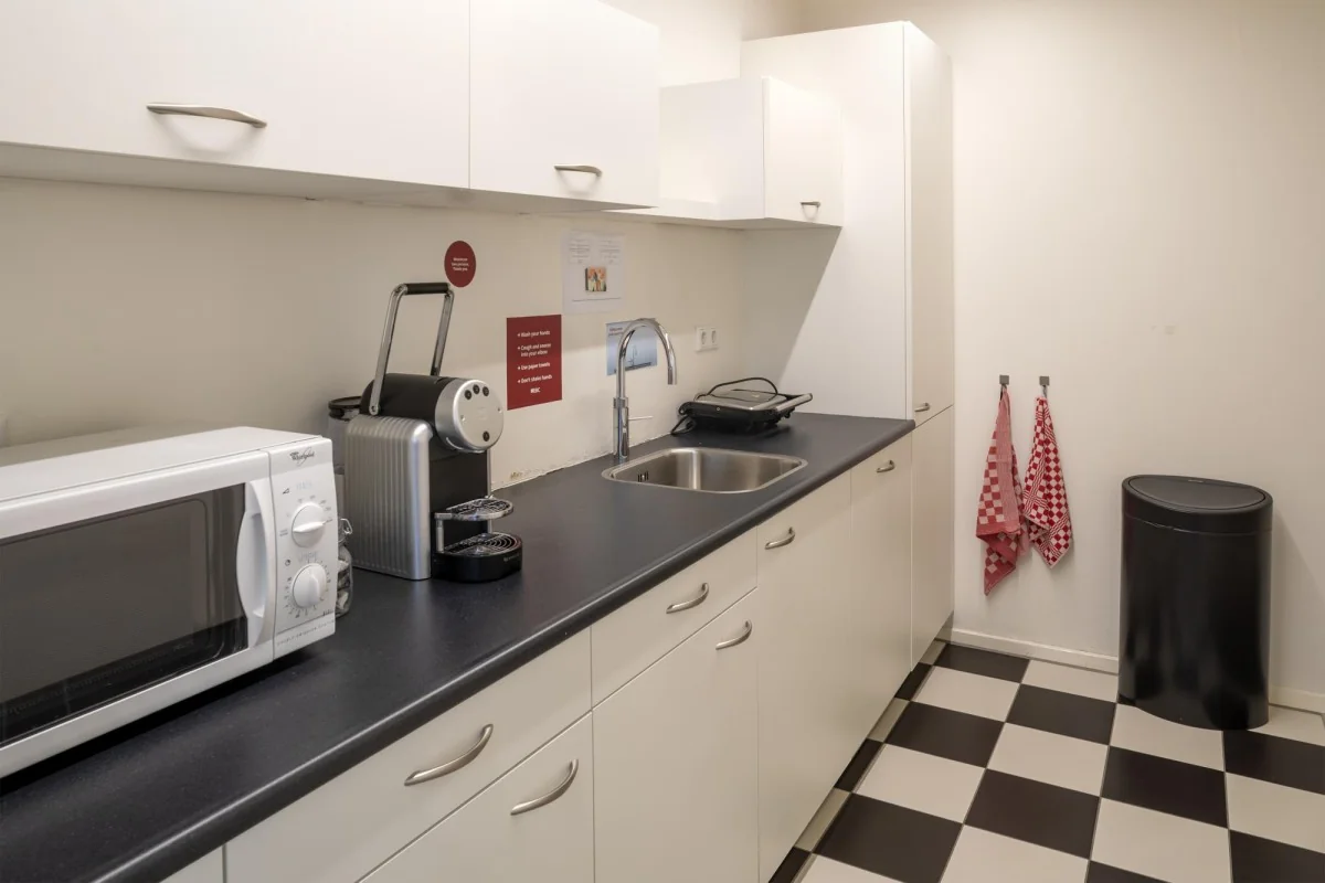 Witte kantoorkeuken aan de Keizersgracht 97 met zwarte werkbladen, koffiezetapparaat, magnetron en zwart-wit geblokte vloer.