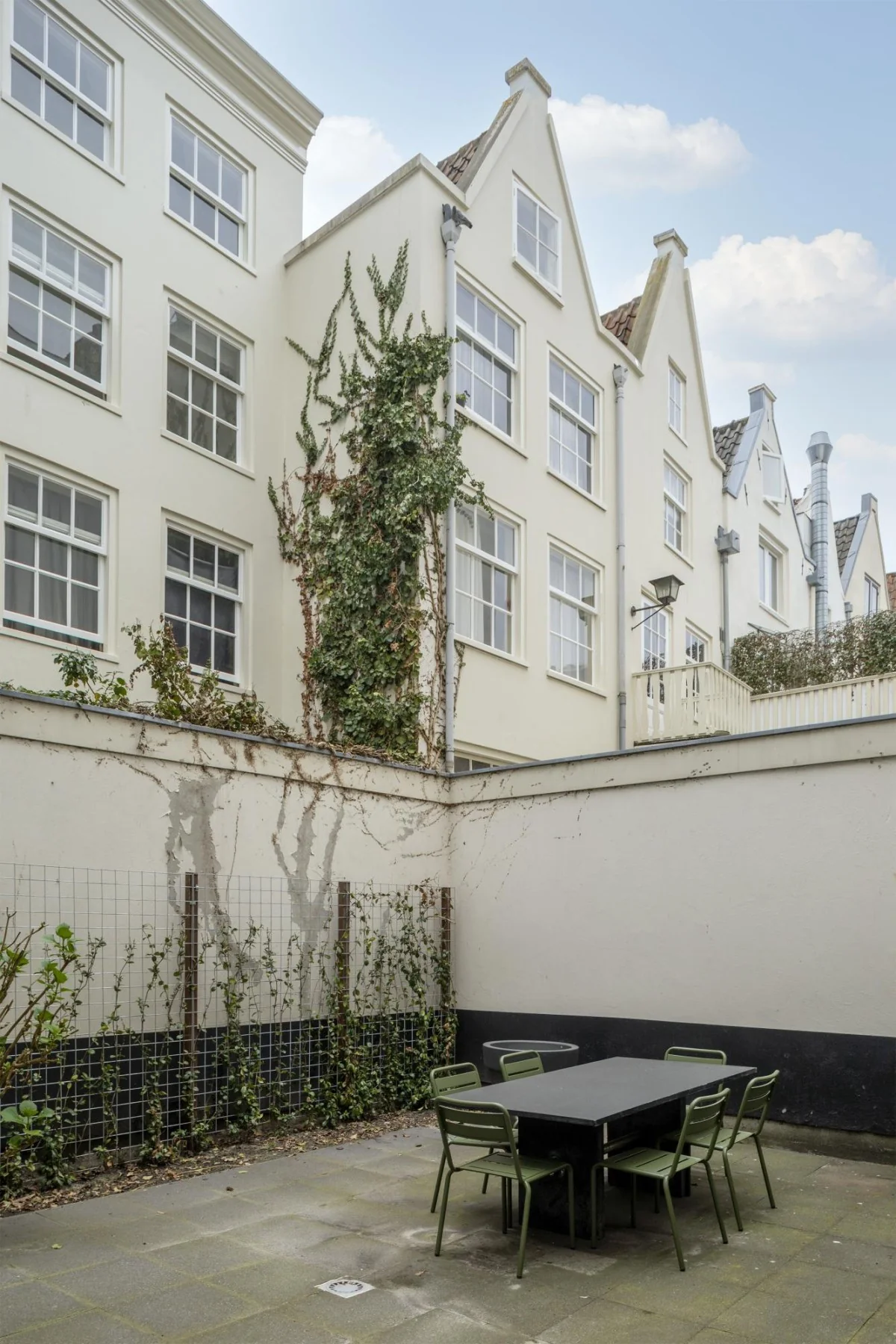 Binnenplaats met eettafel en groene stoelen bij Keizersgracht 97, omringd door lichte gevels met witte kozijnen en klimplanten.