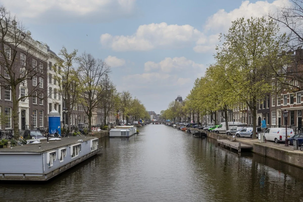 Uitzicht over de Keizersgracht in Amsterdam met woonboten, grachtenpanden en bomen langs het water.
