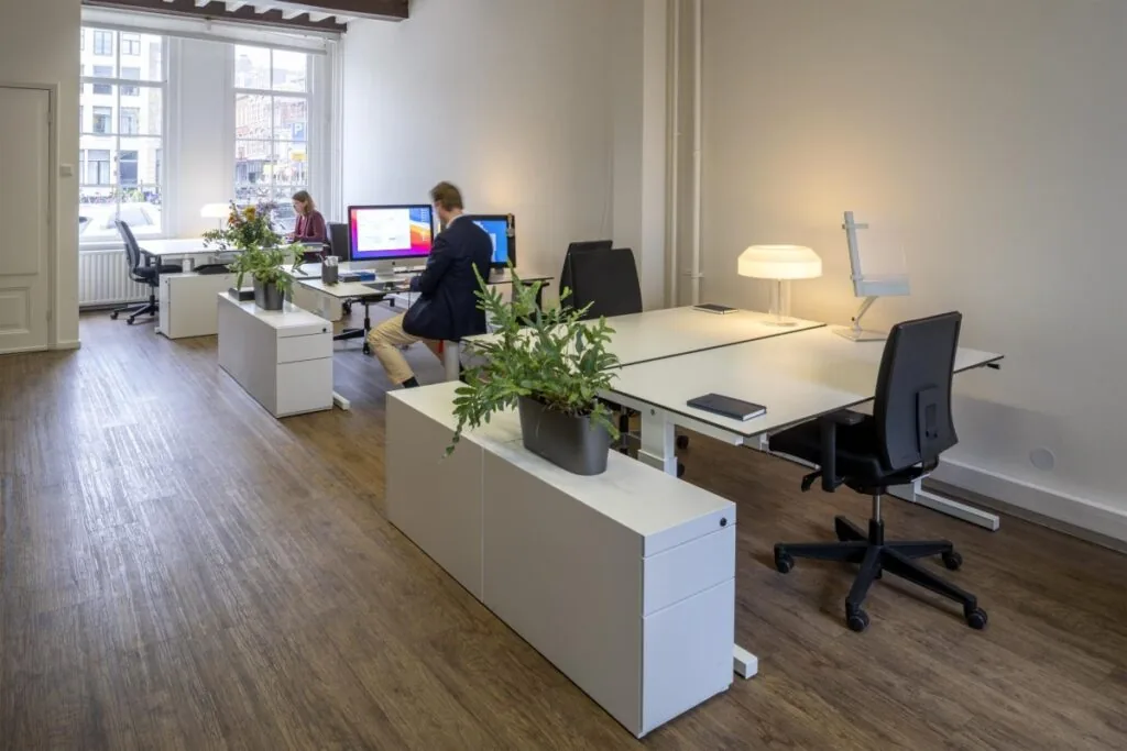 Moderne kantoorruimte aan de Keizersgracht 97 met bureaus, computers, planten en twee werkende personen.