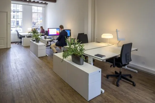 Moderne kantoorruimte aan de Keizersgracht 97 met bureaus, computers, planten en twee werkende personen.