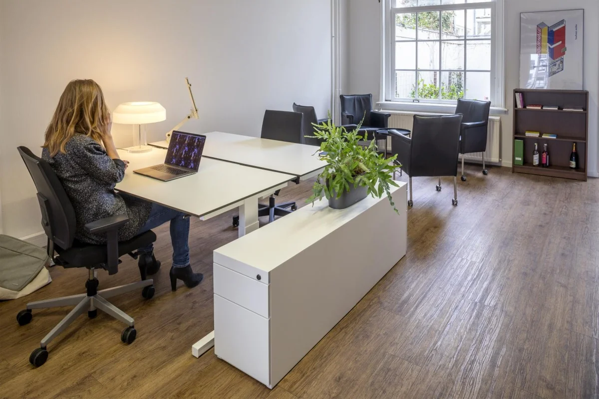Moderne kantoorruimte op Keizersgracht 97 met bureaus, stoelen, planten en een zithoek bij het raam.