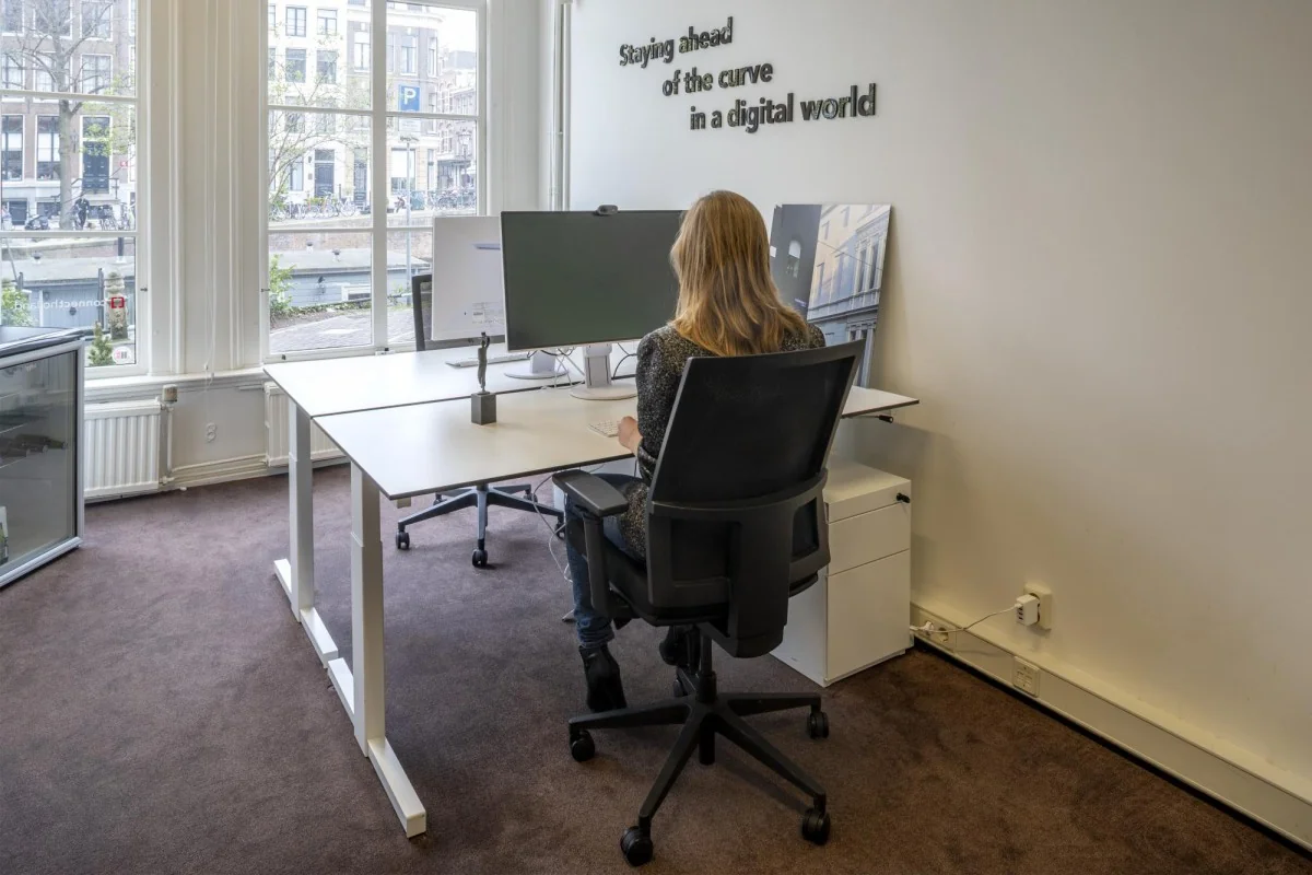 Vrouw werkt op kantoor aan Keizersgracht 97 met zicht op de gracht en grote beeldschermen op het bureau.