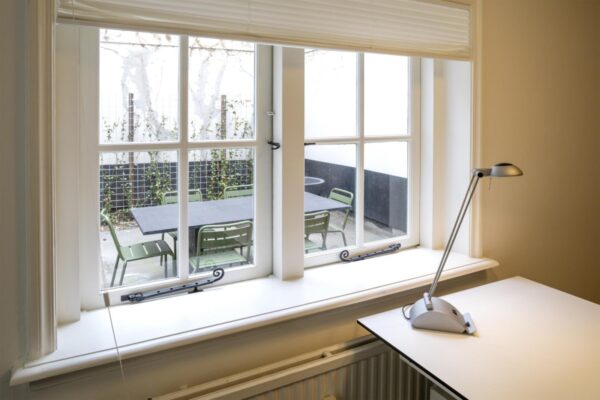 Uitzicht vanuit een kamer op Keizersgracht 97 op een binnentuin met een zwarte buitentafel en groene stoelen.