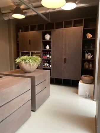 Moderne keuken met donkerhouten kastenwand, open vakken en een kookeiland met een grote plantenpot.