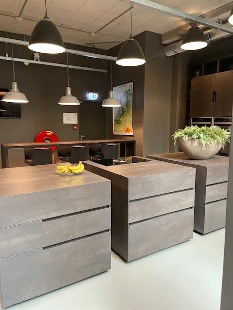Moderne keuken met betongrijze kookeilanden, hanglampen en een grote plantenbak.