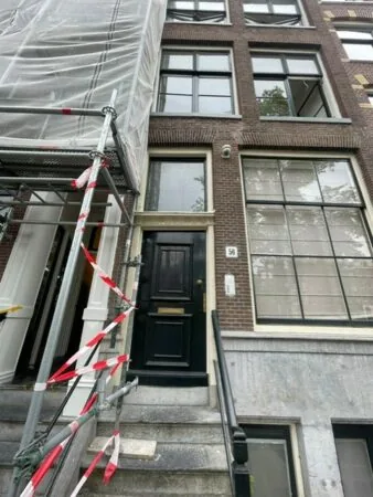 Voorgevel van het pand Kloveniersburgwal 56 met een zwarte voordeur, grote ramen en aangrenzende steiger met afzetlint.