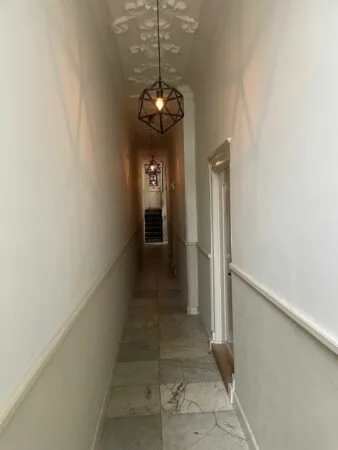 Smalle gang met marmeren vloer, sierplafond en hanglampen in het pand aan de Kloveniersburgwal 56.