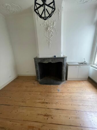 Interieur van een kamer aan de Kloveniersburgwal 56 met een sierlijk gestuukte schouw, houten vloer, moderne hanglamp en een kleine gootsteen met kastje.