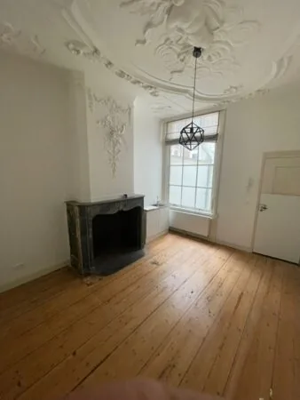 Klassieke kamer in Kloveniersburgwal 56 met houten vloer, sierlijke plafondornamenten en een marmeren schouw.