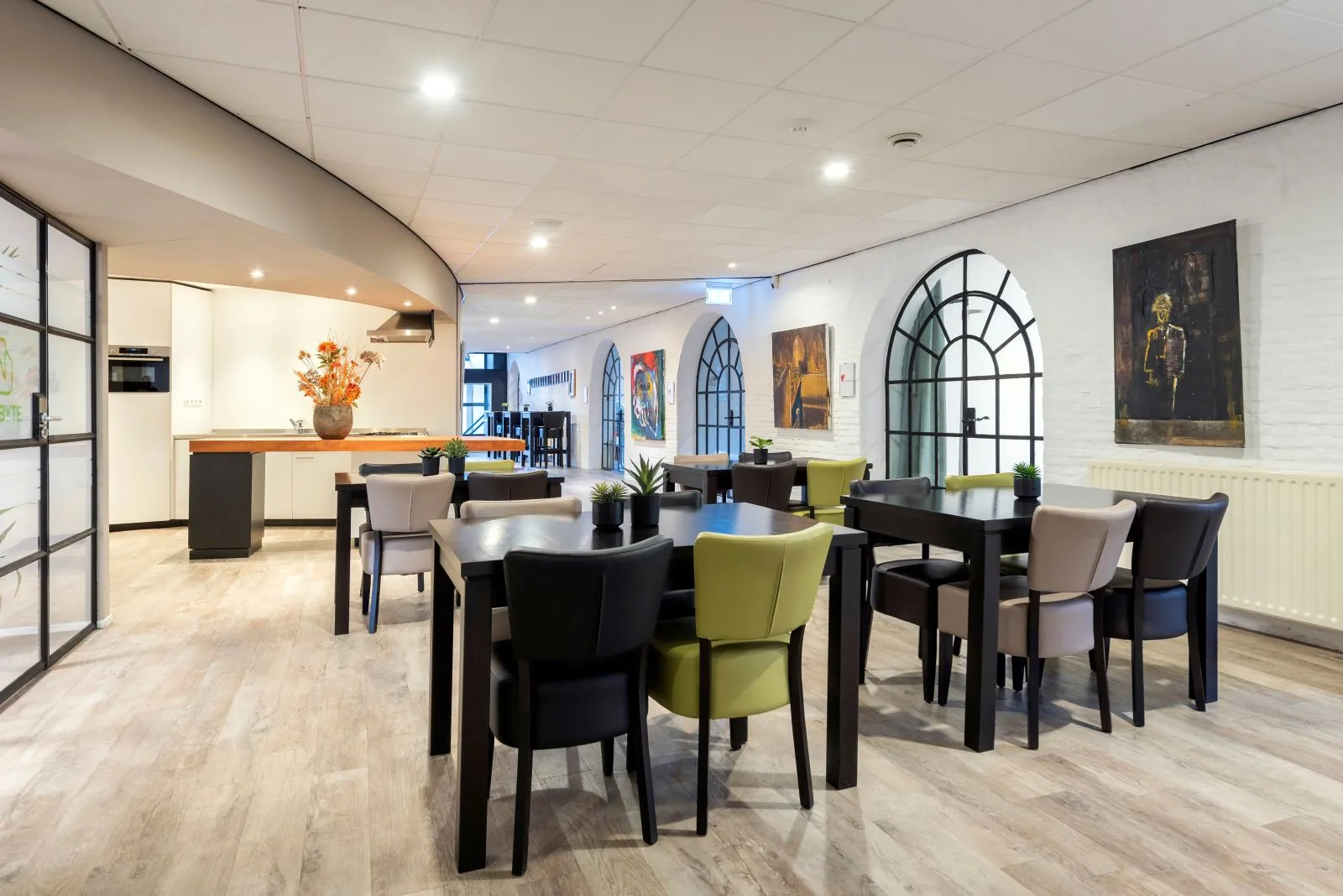 Modern ingericht koffieplein met tafels, kleurrijke stoelen, kunst aan de muur en een open keukenhoek.