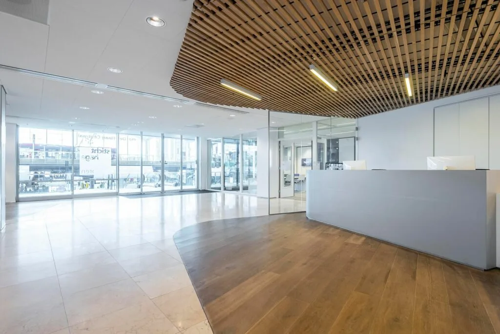Moderne ontvangsthal met houten plafondaccenten, een strakke receptiebalie en glazen wanden in Koningin Juliana Plein 10.