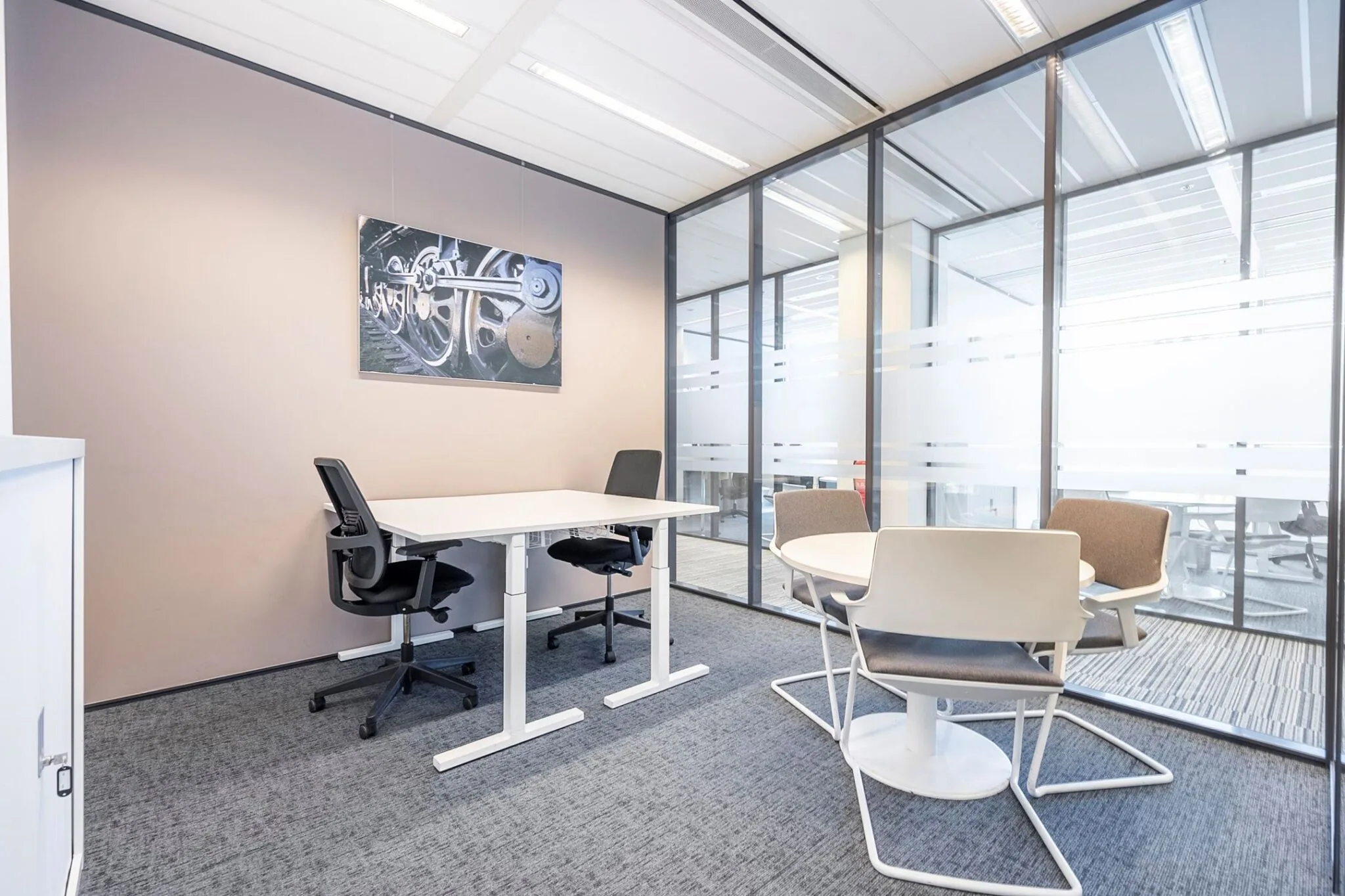 Moderne vergaderruimte in Koningin Juliana Plein 10 met glazen wanden, witte kantoormeubels en een industriële kunstfoto aan de muur.