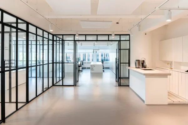 Modern kantoorinterieur aan het Koningin Wilhelminaplein 13 met glazen vergaderruimtes en een minimalistische witte keuken.