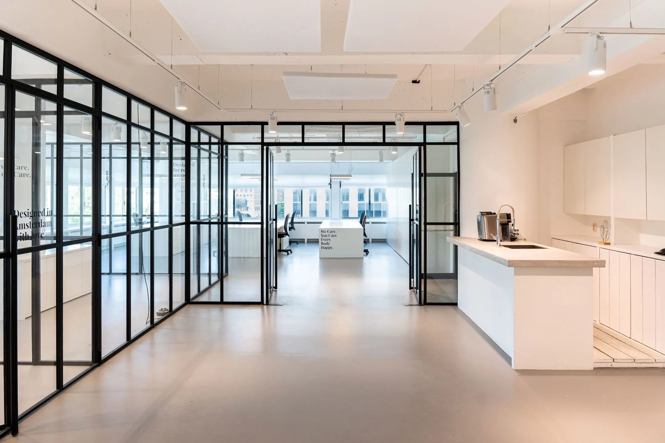 Modern kantoorinterieur aan het Koningin Wilhelminaplein 13 met glazen vergaderruimtes en een minimalistische witte keuken.