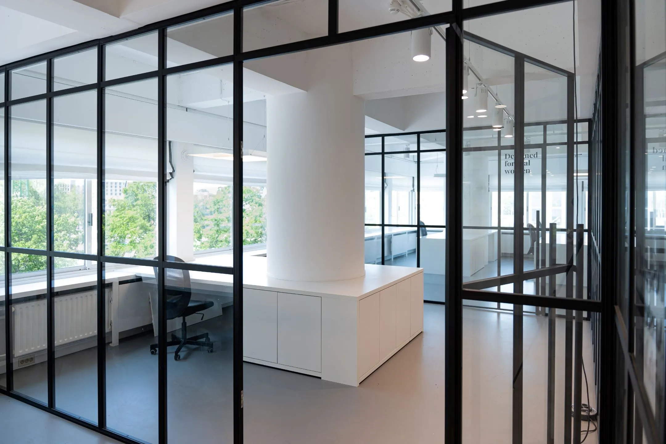 Modern kantoorinterieur met glazen wanden op Koningin Wilhelminaplein 13, met uitzicht op groene bomen.