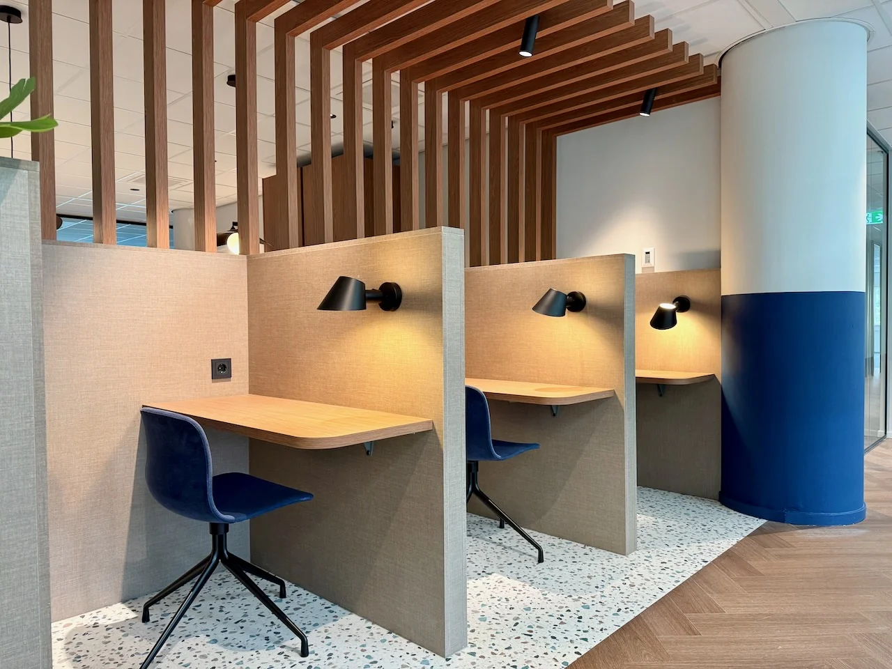 Drie moderne flexwerkplekken met houten bureaus en blauwe stoelen in Kronenburg Offices.