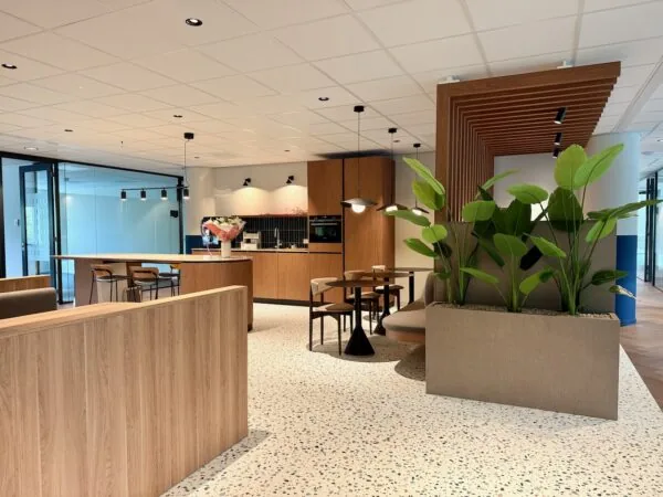 Moderne lounge- en keukenzone in Kronenburg Offices met houten accenten, planten en zitgelegenheid.