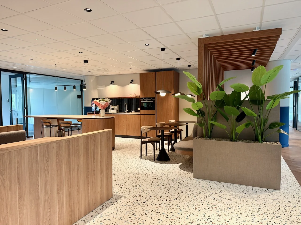 Moderne lounge- en keukenzone in Kronenburg Offices met houten accenten, planten en zitgelegenheid.