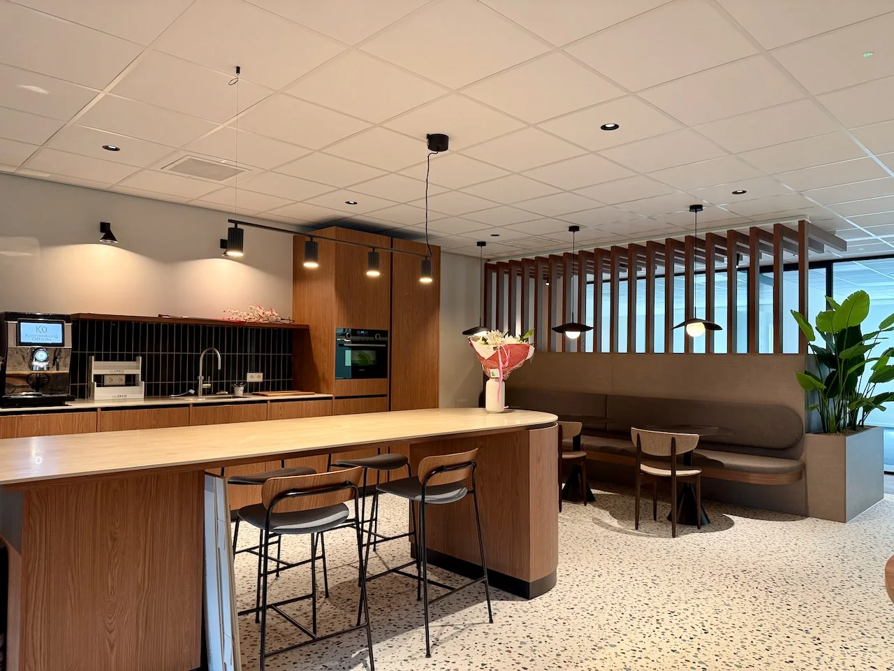 Moderne lounge en kitchenette in Kronenburg Offices met houten afwerking, zitgedeelte en een bos bloemen op de tafel.