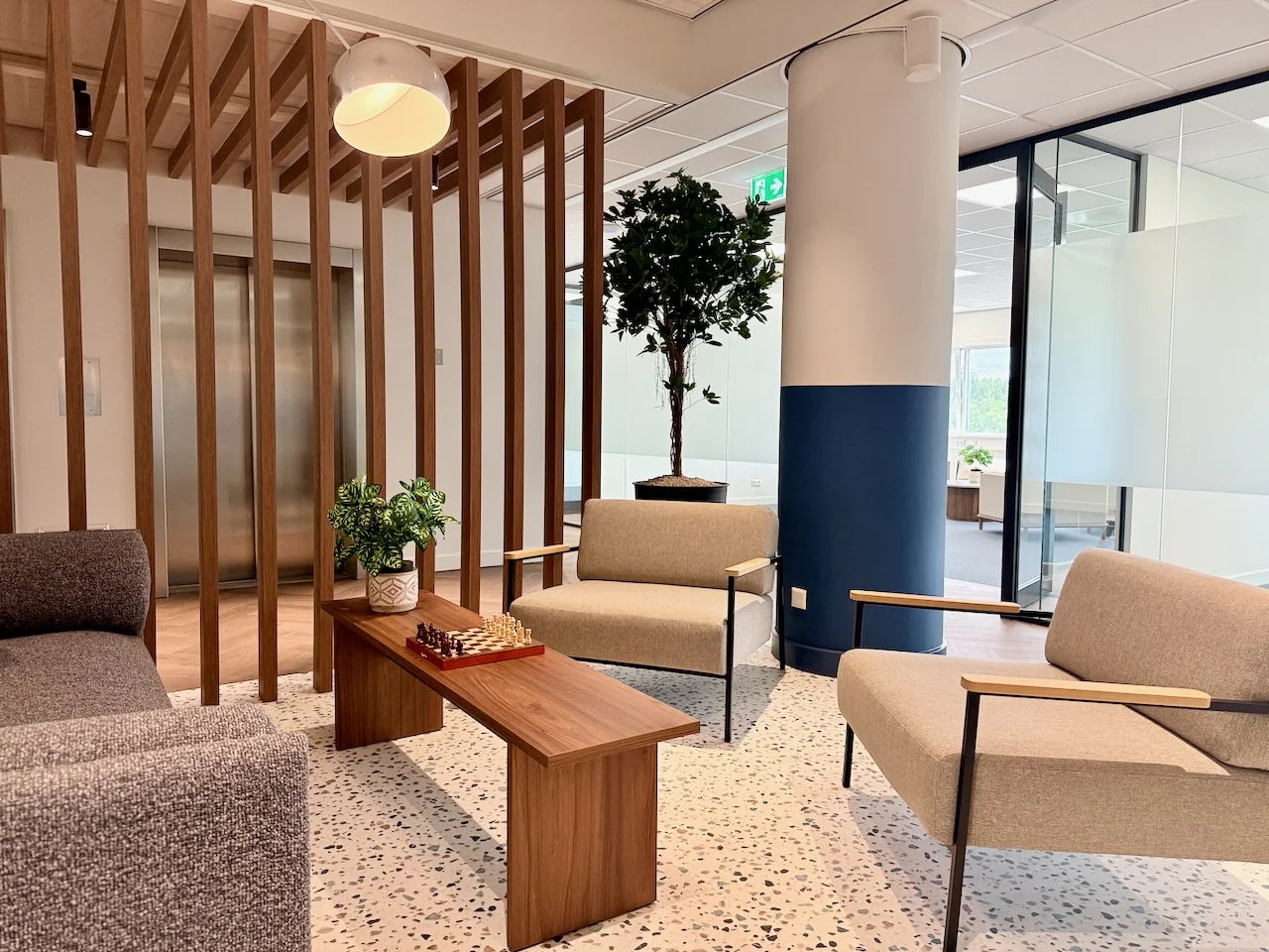 Moderne lounge in Kronenburg Offices met stijlvolle zitmeubels, houten accenten en een schaakbord op de salontafel.