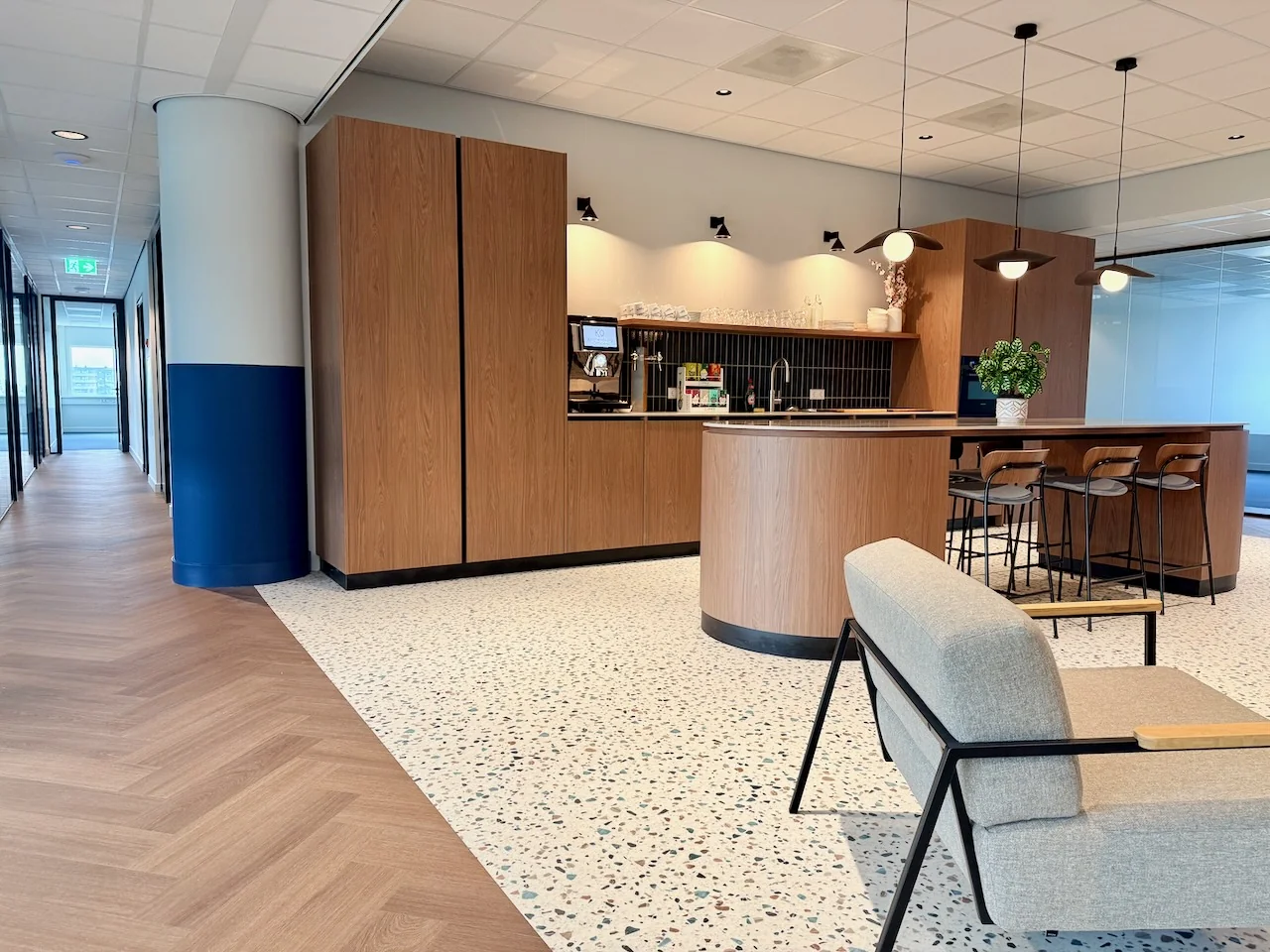 Moderne lounge op de 6e verdieping van Kronenburg Offices met houten keuken, hoge stoelen en een zitgedeelte.