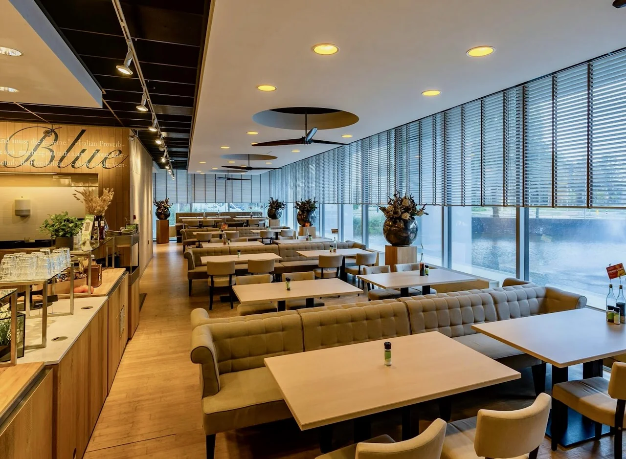 Modern restaurantinterieur met beige zitbanken en grote ramen in Kronenburg Offices Amstelveen.