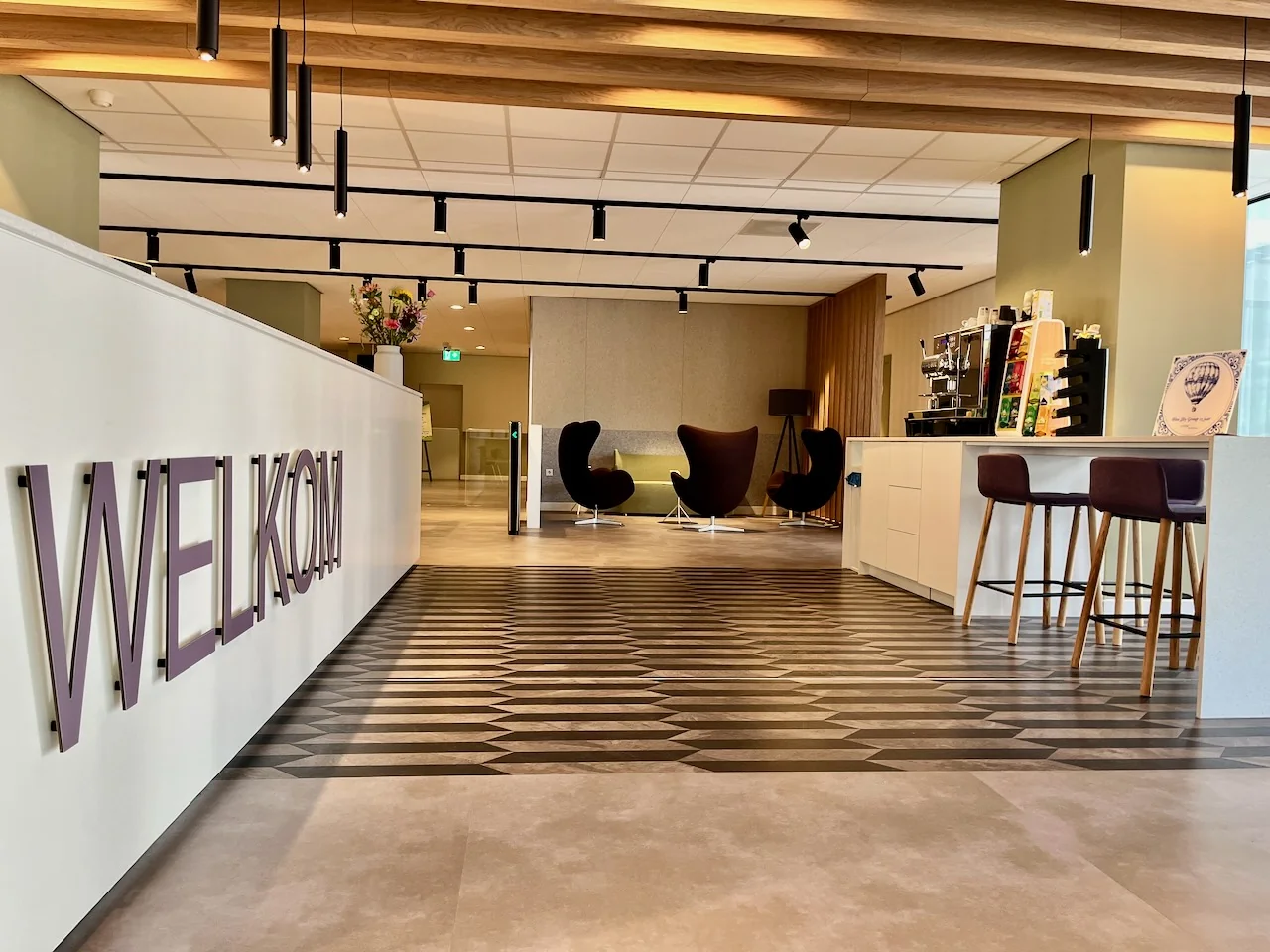 Moderne entree van Kronenburg Offices Ingang 3 met welkomsbord, zitgedeelte en koffiemeubel.