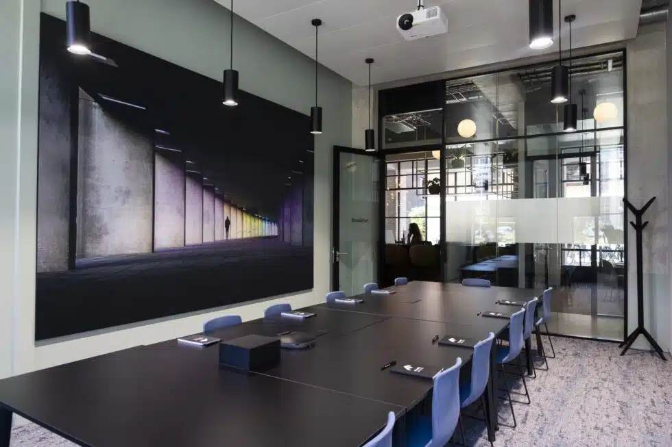 Een moderne vergaderruimte met zwarte stoelen en tafels, en een groot kunstwerk aan de muur.