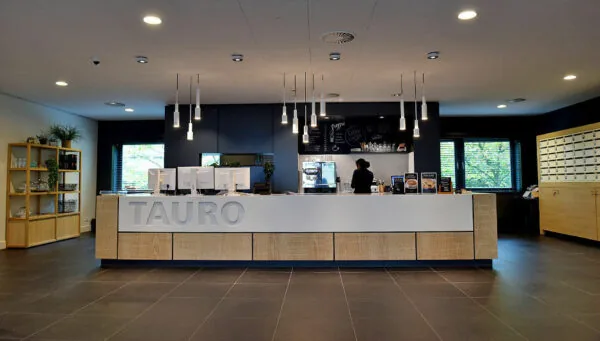Moderne receptiebalie van TAURO aan de Laan van Vredenoord 33 met een koffiecorner en een medewerker op de achtergrond.