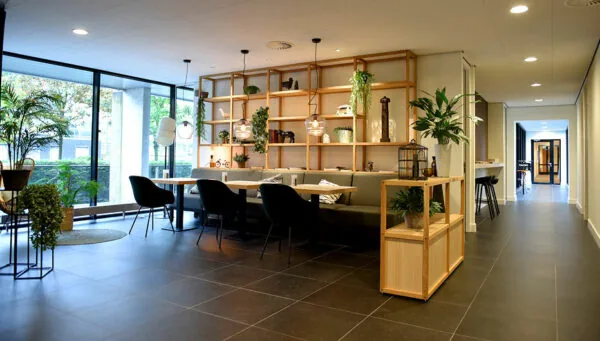 Moderne en sfeervol ingerichte wachtruimte met planten, zitplekken en houten open wandkast in Laan van Vredenoord 33.