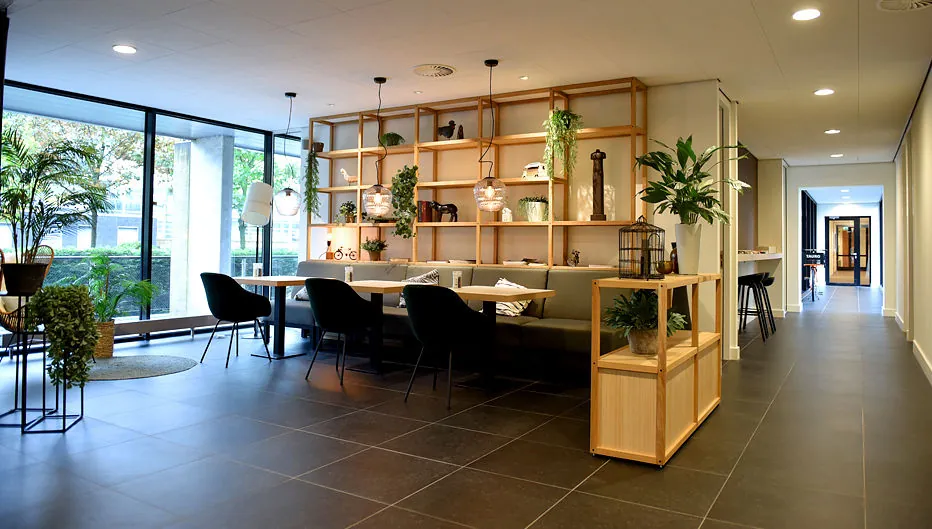 Moderne en sfeervol ingerichte wachtruimte met planten, zitplekken en houten open wandkast in Laan van Vredenoord 33.