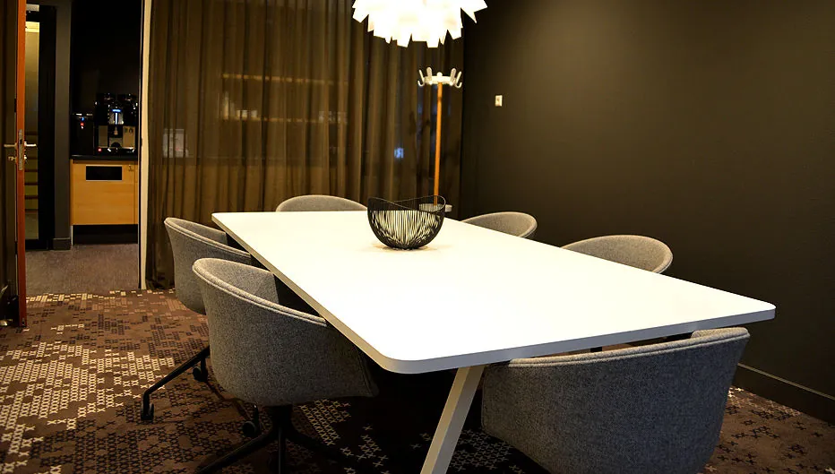 Vergaderruimte met een witte tafel, zes grijze stoelen, een moderne hanglamp en een zwarte schaal, gelegen aan de Laan van Vredenoord 33.